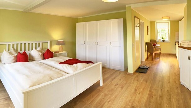 A bedroom with a bed, nightstands, a wardrobe, and a small dining area.