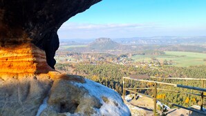 A rock formation with a view of a town and forested hills in the background.