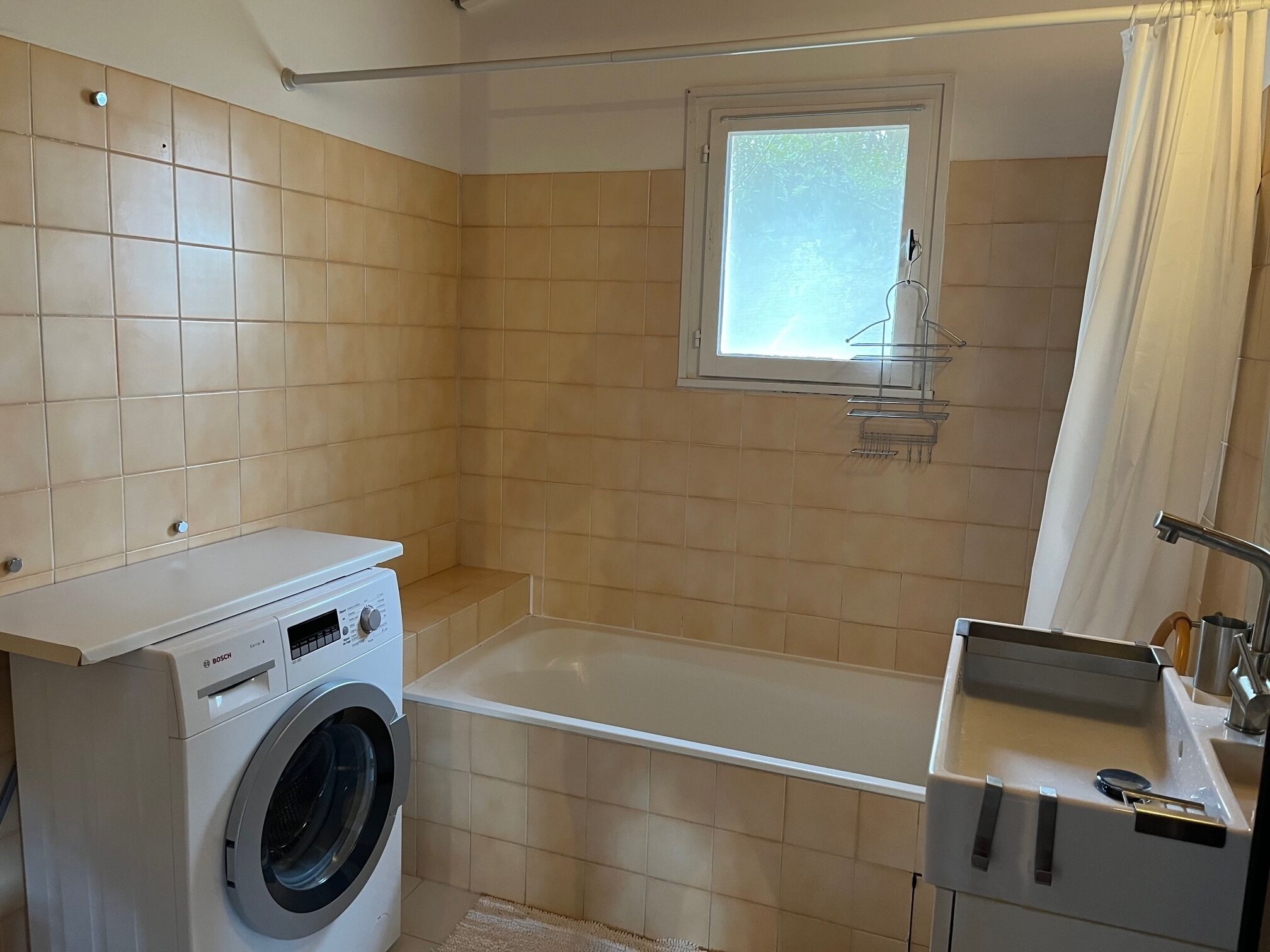 Une petite salle de bain équipée d’un lave-linge, d’une baignoire et d’une petite fenêtre.