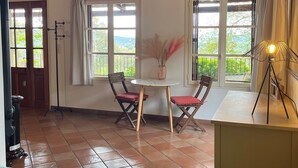 A room with a wooden ceiling, two windows with curtains, a table with chairs, and a bed with a green floral bedspread. - Maison Individuelle au Cœur du Maquis Corse (Porto-Vecchio)