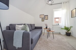 Una sala de estar moderna con un sofá gris, una mesita de madera y un ventanal con cortinas blancas.