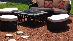 An outdoor seating area with a covered sofa, two round tables, and a fire pit. - Big bang in a little boxx (Warren)