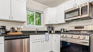 A modern kitchen with white cabinets, a stainless steel dishwasher, a built-in oven, and a microwave. - Big bang in a little boxx (Warren)