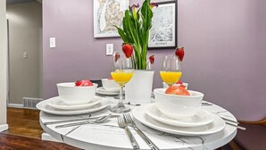 A dining table set with white plates, bowls, and cutlery, accompanied by glasses of orange juice and a vase with green leaves and strawberries. - Big bang in a little boxx (Warren)