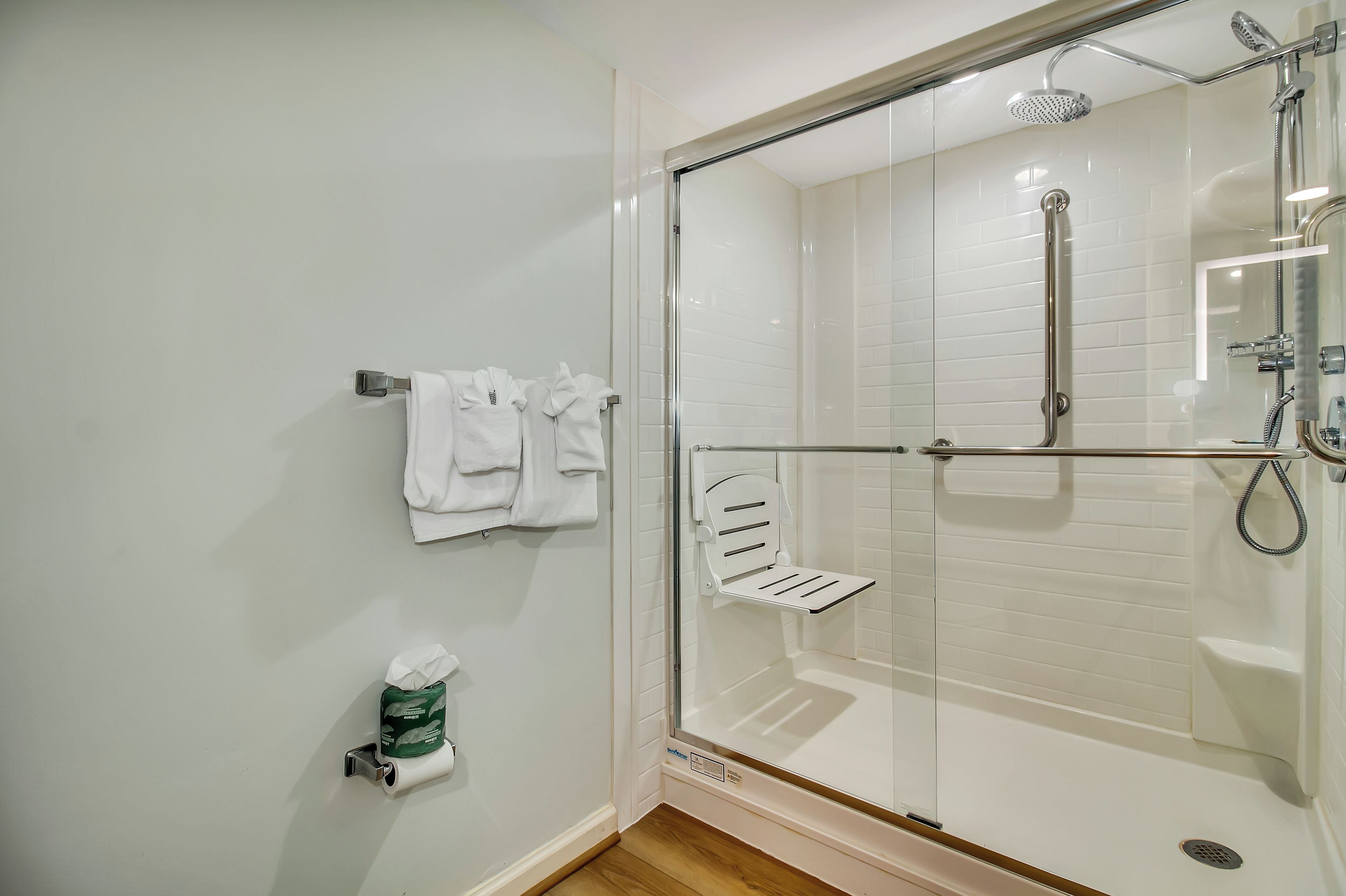 Un baño moderno con ducha envuelta en vidrio, paredes de azulejos blancos y un perchero con toallas.