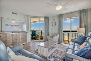 Een ruime woonkamer met een grote televisie, een bank, een salontafel en een balkon met uitzicht.
