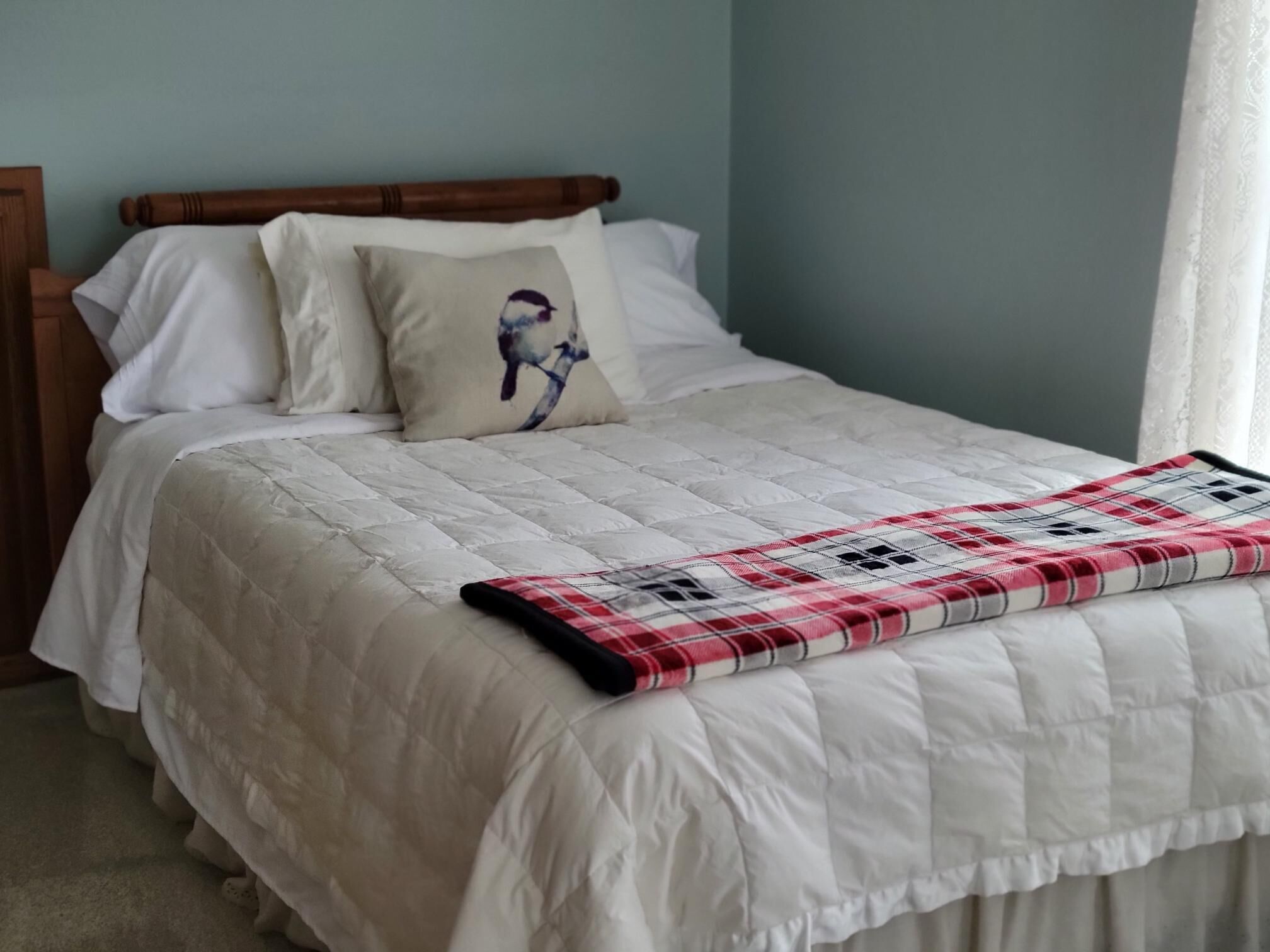 Una cama bien hecha con colcha y manta escocesa, cabecera de madera y almohada con diseño floral.