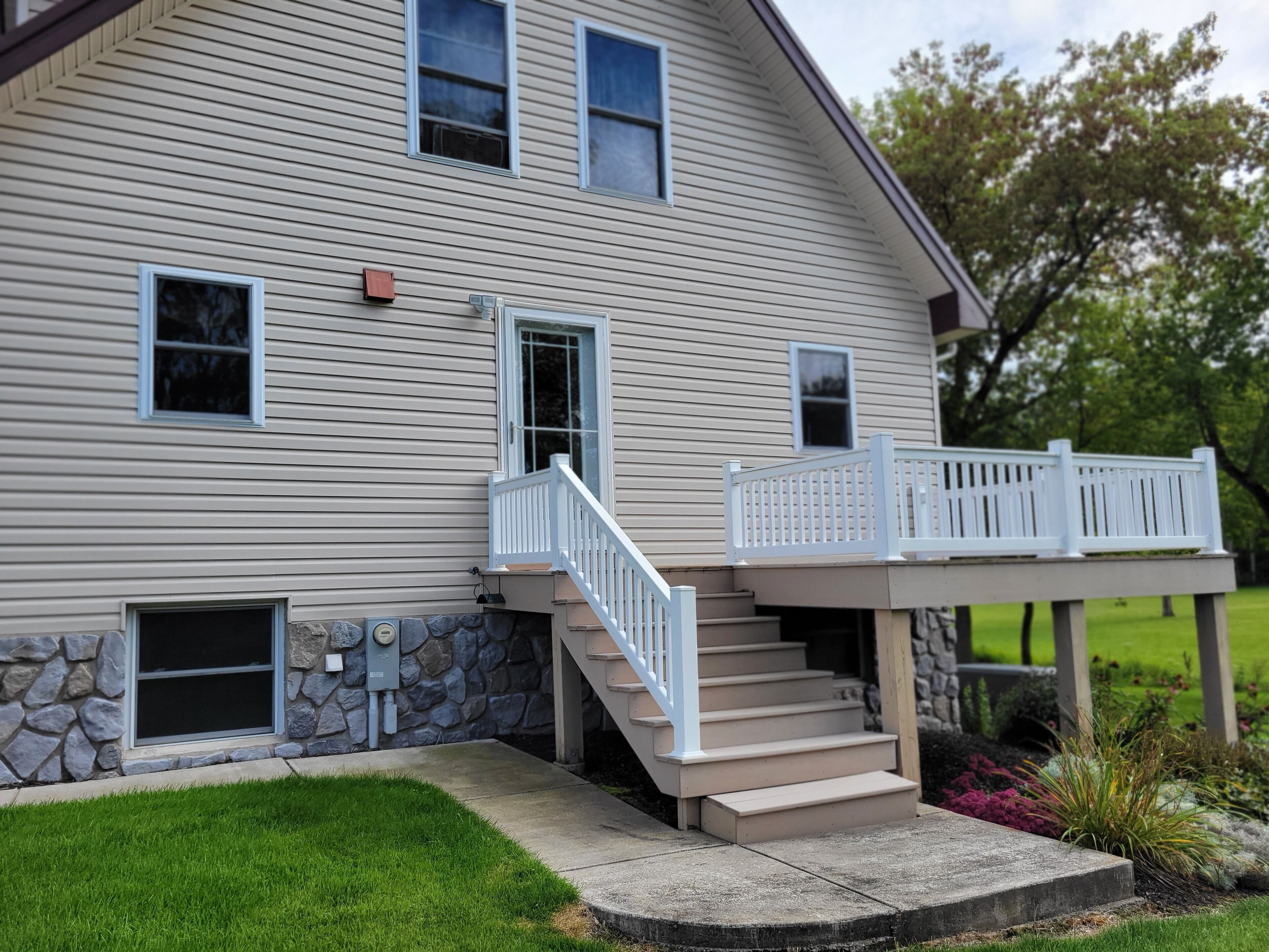 A two-story house with a stone foundation, a front porch with a white railing, and a small set of stairs leading to the entrance.