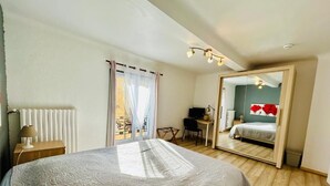 Un dormitorio con una cama grande, un escritorio, una silla, un espejo y vistas a otra habitación.