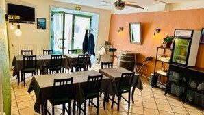Un comedor con varias mesas y sillas, un ventilador de techo, un televisor y un refrigerador.