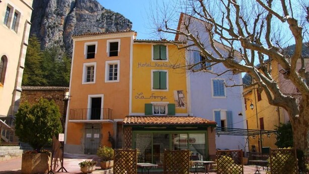 Un edificio amarillo con un letrero que dice "Hotel Restaurant La Forge" y mesas al aire libre.