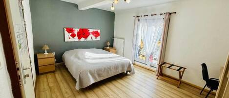 A bedroom with a bed, a nightstand, a lamp, a chair, a window with curtains, and a wall painting.