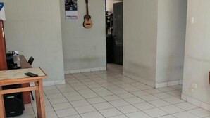 Um quarto espaçoso com chão de azulejos, uma mesa de madeira e uma guitarra pendurada na parede.