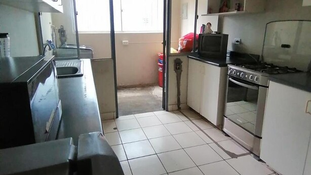 Cozinha com fogão, forno e pia. Uma porta deslizante dá acesso a uma varanda.