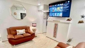 Un salon moderne avec un canapé en cuir marron, un téléviseur à écran plat fixé au mur, un miroir décoratif et une petite table avec une lampe.