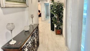 A hallway with a marble floor, a wooden console table with decorative items, a large framed painting, a potted plant, and a door leading to another room. - Feel at home ! Only 5 min from the Beach ! (Clearwater)