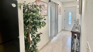 A hallway with a refrigerator, a potted plant, a door with a window, and a decorative item on a console table. - Feel at home ! Only 5 min from the Beach ! (Clearwater)