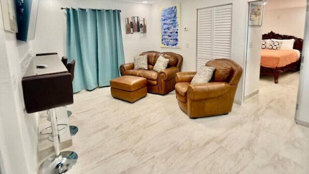 A living room with two leather armchairs, a small table, and a TV mounted on the wall. - Feel at home ! Only 5 min from the Beach ! (Clearwater)
