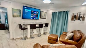 A modern living room with a leather sofa, a TV mounted on the wall, and a bar area with stools. - Feel at home ! Only 5 min from the Beach ! (Clearwater)