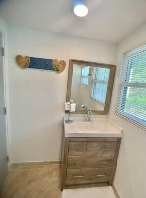 A bathroom with a wooden vanity, a mirror, and a window with blinds.