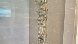 A shower with a tiled wall, a showerhead, and a handrail.