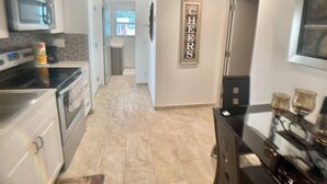 A modern kitchen with stainless steel appliances, a tiled floor, and a 'CHEERS' sign on the wall.