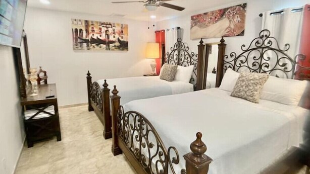 A hotel room with two beds, a ceiling fan, a desk, and artwork on the walls.