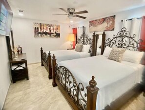 A hotel room with two beds, a ceiling fan, a desk, and artwork on the walls.