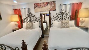A hotel room with two beds, each with a decorative headboard, a painting above the beds, and a ceiling fan.