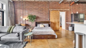 Ein modernes Schlafzimmer mit einer Ziegelwand, einem hölzernen Bettgestell, einem grauen Sofa und einem kleinen Beistelltisch.