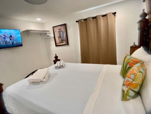 Ein Hotelzimmer mit einem Bett, einem Fernseher, einem gerahmten Bild an der Wand und einem Vorhang.