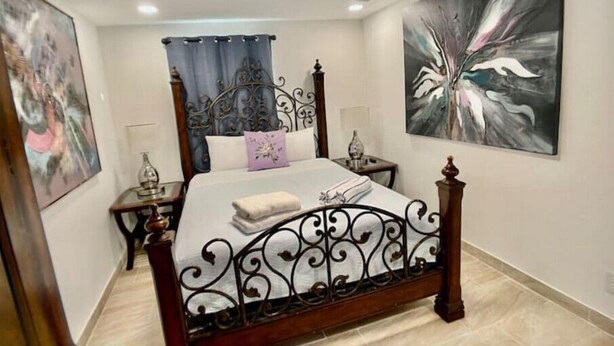 A bedroom with a four-poster bed, a nightstand, a bedside table, and a large abstract painting on the wall. - Loving Apartment! (Clearwater)