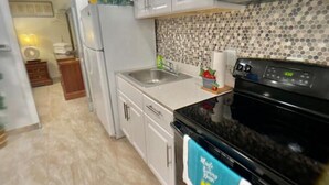 Una cocina compacta con armarios blancos, una estufa negra y un salpicadero de azulejos.