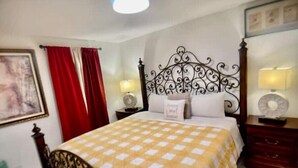 Un dormitorio con cama, mesita de noche, lámpara, espejo y cortina roja.