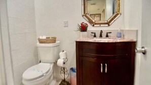 Un baño con inodoro blanco, tocador de madera con espejo y una pequeña cesta sobre el tanque del inodoro.