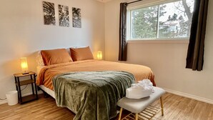 A bedroom with a bed, bedside lamps, a bench, and artwork on the wall. - Spacious 4-BR Home near Jasper! (Hinton)