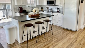 A modern kitchen with white cabinetry, a central island with stools, a stainless steel refrigerator, and a microwave. - Spacious 4-BR Home near Jasper! (Hinton)