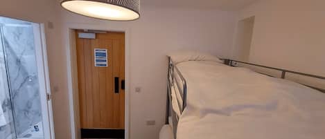 A bedroom with a bunk bed, a wooden door with a fire action sign, a hanging light fixture, and a marble-patterned wall.
