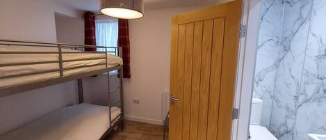 Una habitación pequeña con literas, una puerta de madera y un baño con paredes de mármol.