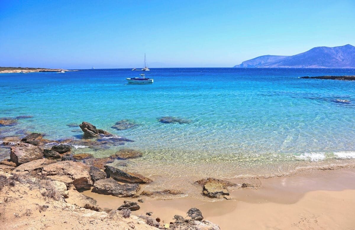 A beach with clear water, rocks, and a boat.