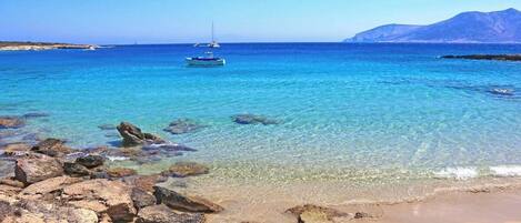 A beach with clear water, rocks, and a boat.