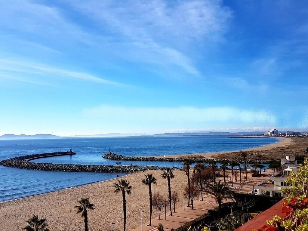 A coastal view with a beach, palm trees, and a clear sky.