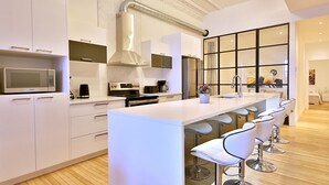 Una cucina moderna con mobili bianchi, un'isola centrale con sgabelli da bar, un'ampia finestra e un forno a microonde integrato.