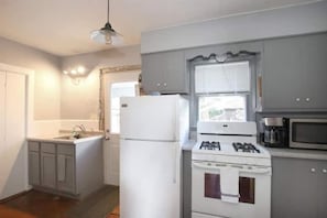 Kitchen area with refrigerator, stove, and microwave, featuring light gray cabinets and a small window above the sink.