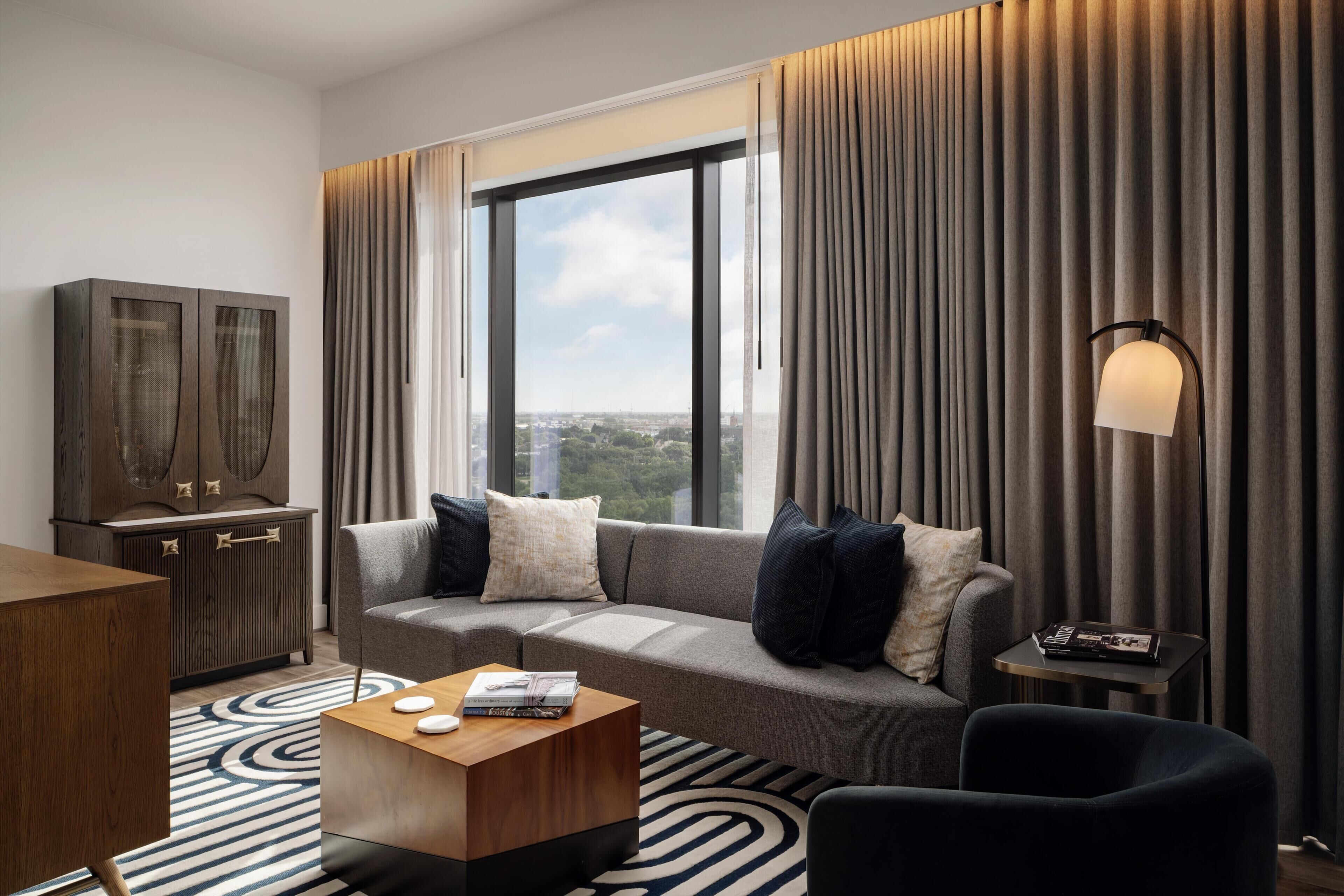 Een moderne hotelkamer met een groot raam, een bank, een salontafel, een bijzettafeltje en een kast.