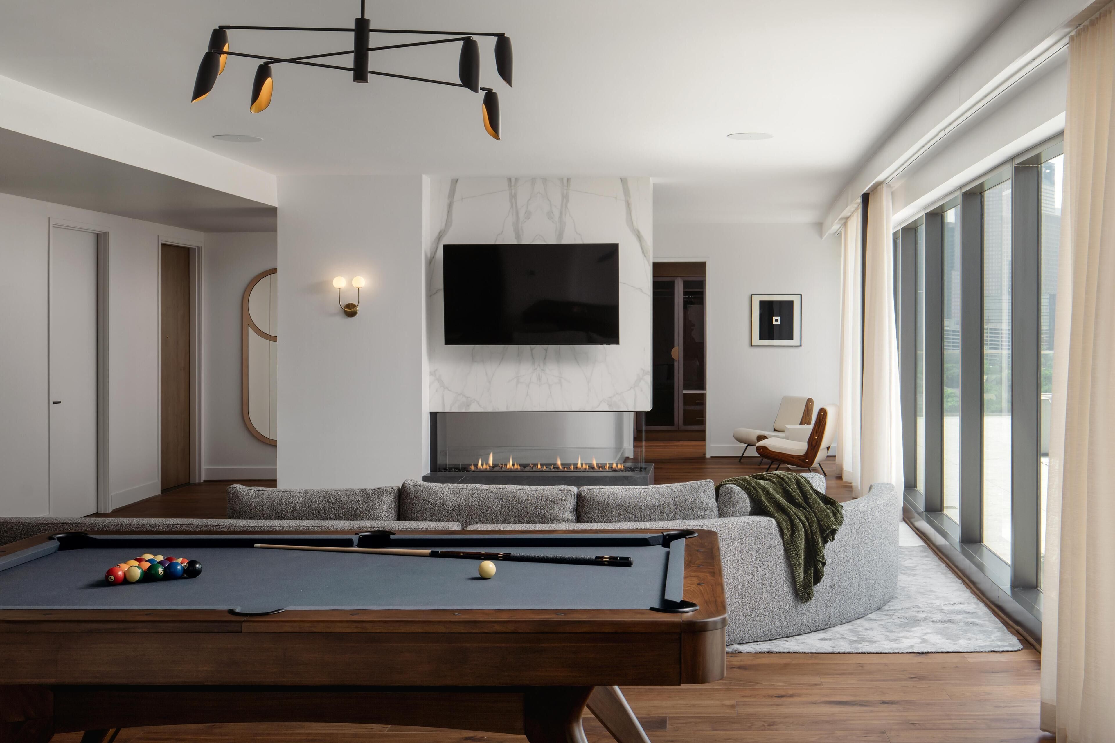 Een moderne woonkamer met een pooltafel, een open haard, een televisietoestel en een groot raam.