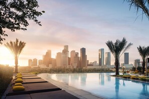 A poolside area with lounge chairs and a city skyline in the background.
