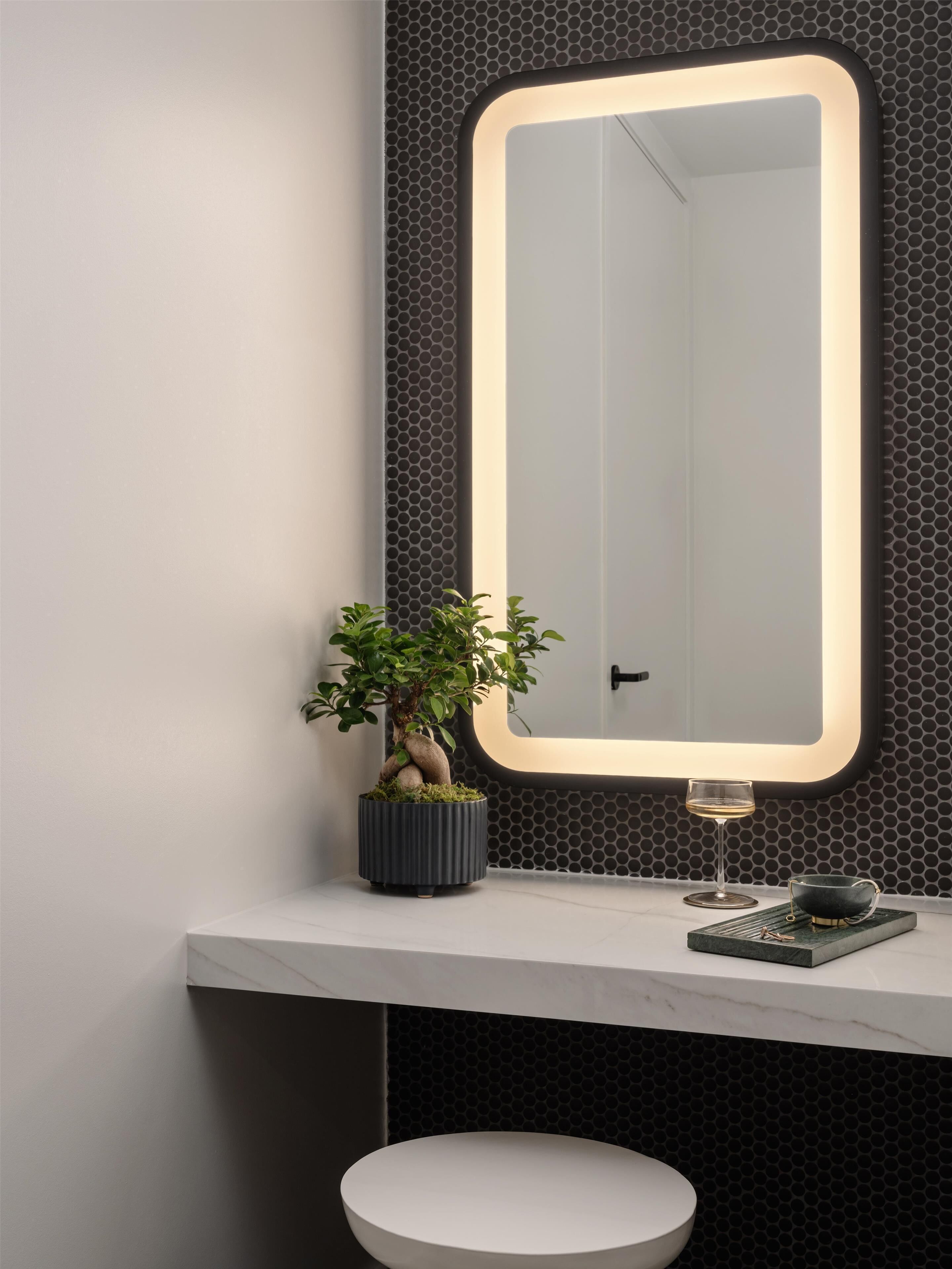 A modern bathroom with a large mirror, a potted plant, a wine glass, and a bowl on the countertop.