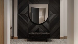 A modern hallway with a geometric patterned wall, a bench, and a large mirror.