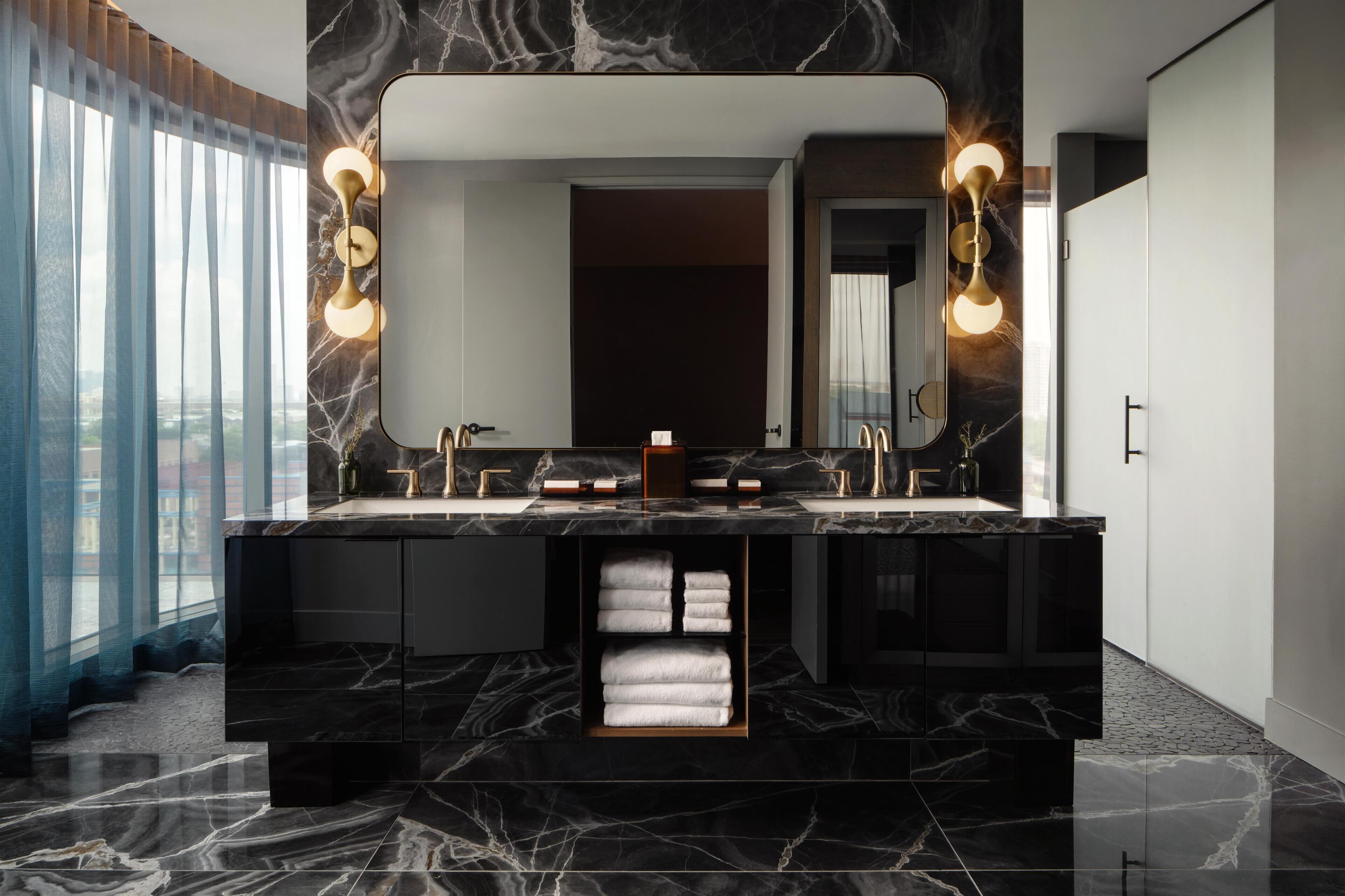 A modern bathroom with a large mirror, dual sinks, and marble countertops.